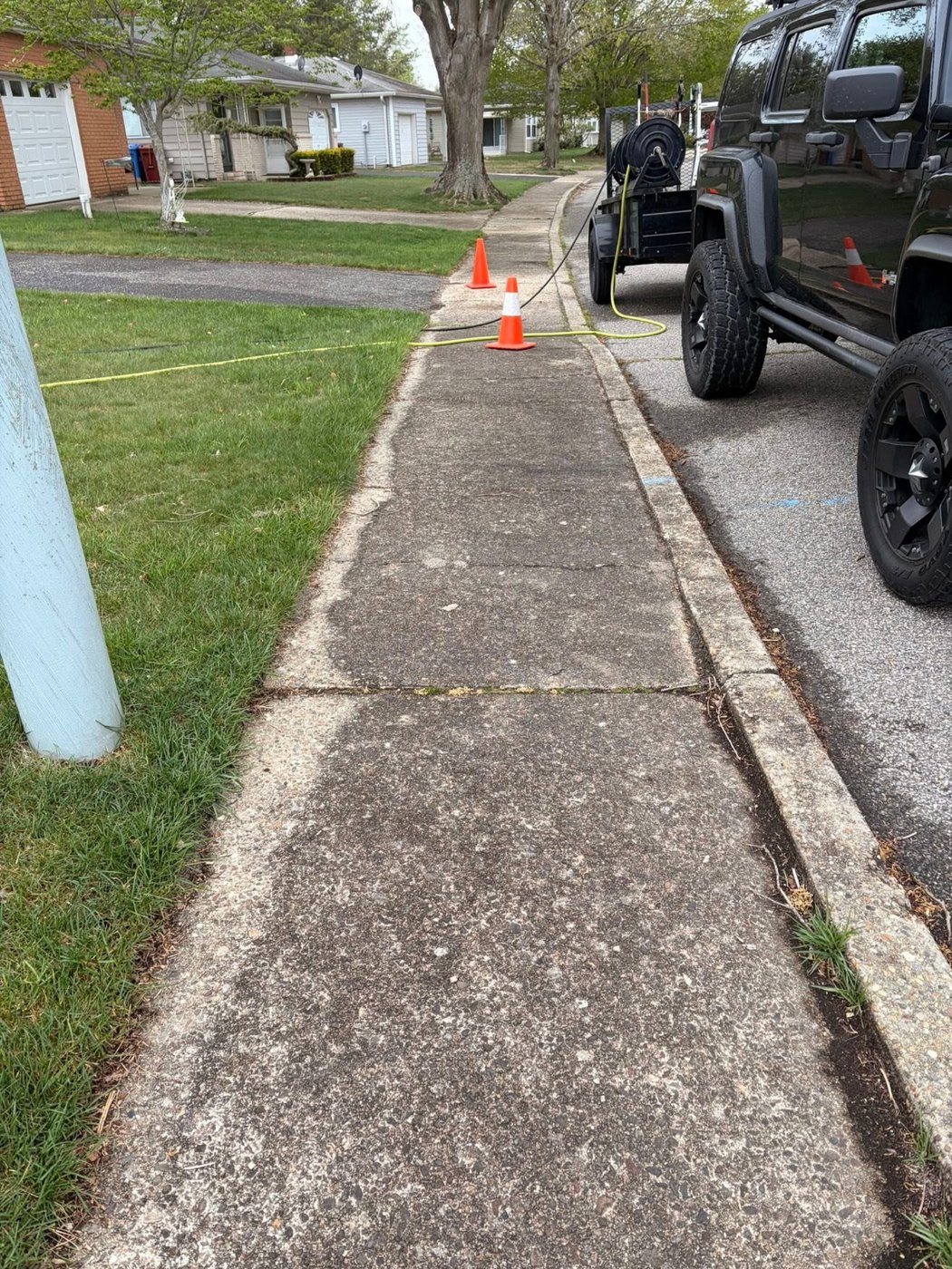Stained, weathered sidewalk with weeds along the curb